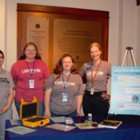 a teacher standing with three high school students, each wearing a t-shirt that reads "careerline tech center; they are stnading in front of a table with items and displays on it from their research on river quality